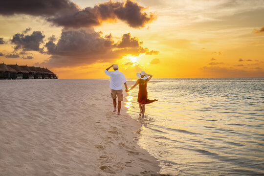 A happy couple holding hands and running down a tropical beach during sunset time in the Maldives islands