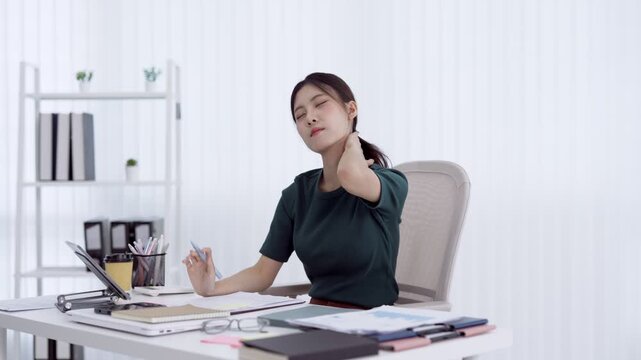 Young Asian office worker experiencing neck pain and discomfort at desk in modern white workspace
