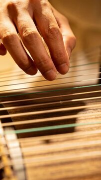 Vertical video: Hovering then descending, hand plucking zither strings in warm studio, making music
