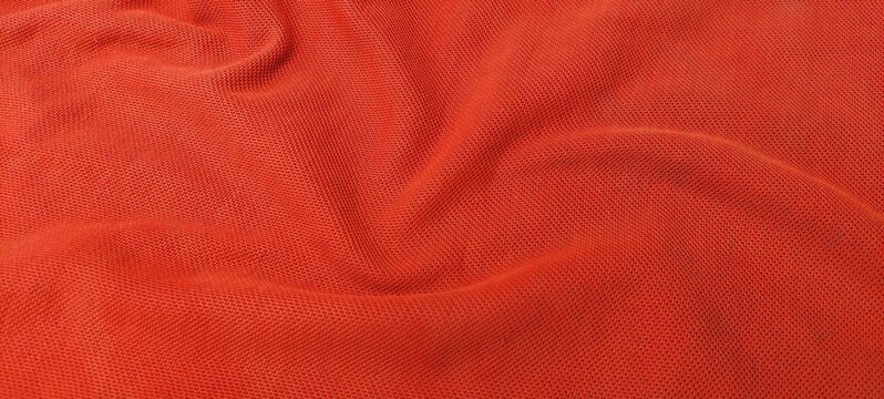 Orange sports clothing fabric in close up with football jersey texture. Soft textile sports wear background featuring detailed orange football shirt material.