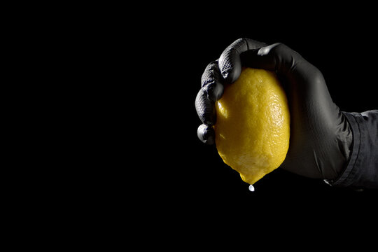 Hand in black glove squeezing last drop from lemon concept of extreme margin squeeze