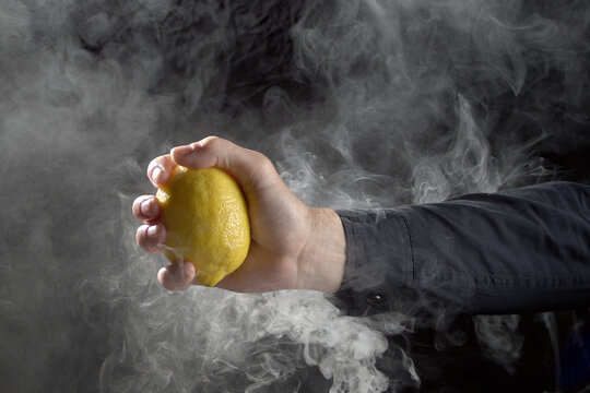 Male hand firmly holding whole yellow lemon surrounded by thick smoke concept of risk management