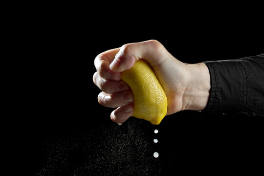 Male hand strongly crushing yellow lemon extracting juice drops on dark background concept of margin squeeze