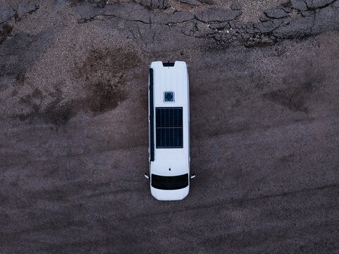 Aerial view of a white camper van with a solar panel on the roof parked on a gravel surface in Latvia.