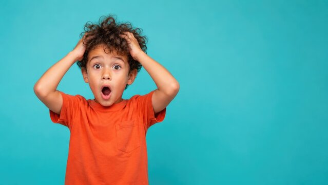 Shocked little boy holding head with surprised expression on blue background