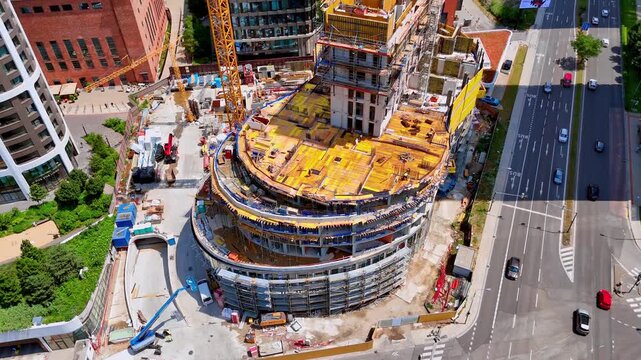 Curved high rise building foundation on active construction site, Bratislava, Slovakia. Elevated perspective of multi story concrete levels, yellow formwork and wide city street.