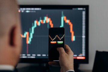 Fototapeta premium Close up of trader hand holding smartphone, using trading app with stock market charts for financial analysis and monitoring investment data.