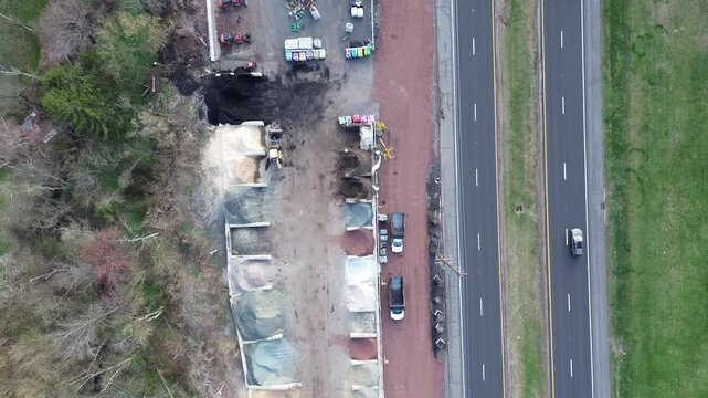 Industrial landscape supply site along US 202 in Readington Township near creek side forest. Colorful grayscale aggregates, mulch piles organize dirt lot under crisp daylight in Flemington, NJ