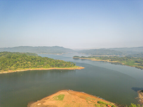 Aerial view of Wadaslintang Reservoir featuring lush green hills, calm water, and agricultural fields along the shoreline in Wadaslintang, Central Java, Indonesia.