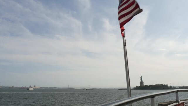 Statue of Liberty on Liberty Island, New York, United States. Cooper monument, symbol of democracy and patriotism near Manhattan, NYC USA. American flag waving in wind on ferry boat, tourist cruise.