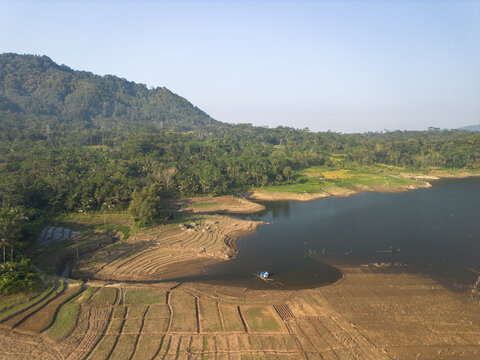 Aerial view of the Karanganyar reservoir area, featuring terraced agricultural fields, lush green hills, and calm water in Wadaslintang, Central Java, Indonesia.