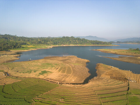 Aerial view of the Karanganyar reservoir surrounded by terraced agricultural fields and lush green hills in Wadaslintang, Central Java, Indonesia.