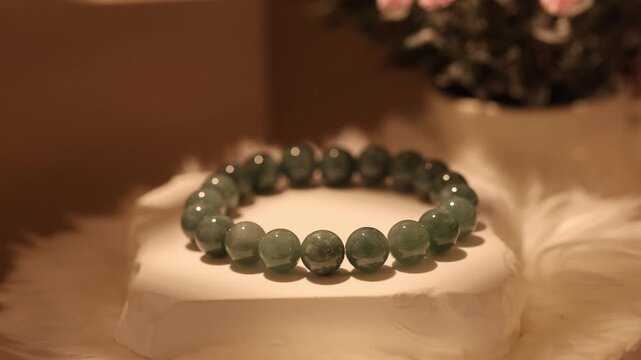 A Burmese jade stone bracelet placed on a rotating display stand. The bracelet is highlighted with gentle lighting against a soft background.