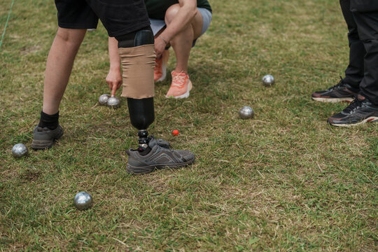 A close up shot of a man with a prosthetic leg playing petanque on grass. Veteran rehabilitation, adaptive sports game, outdoor recovery in Ukraine.