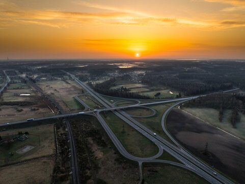 Aerial view of the A5 and A8 highway interchange at sunrise, featuring surrounding fields and forests in Olaine parish, Olaine Municipality, Latvia.