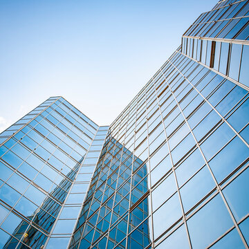 Modern Glass Skyscraper. Low angle view of contemporary corporate office building reflecting a blue sky with clouds.
