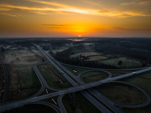 Aerial view of the A5 and A8 highway interchange at sunset with golden light over the surrounding fields and forests in Olaine parish, Olaine Municipality, Latvia.