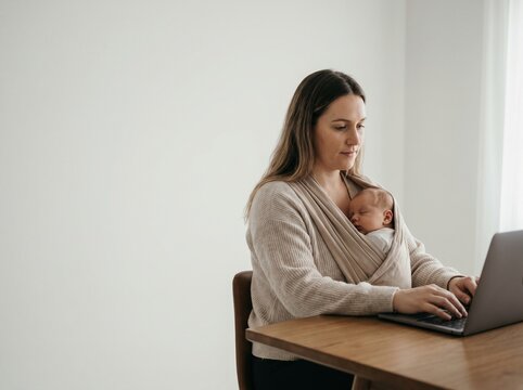 Working mother uses laptop while baby sleeps in a carrier