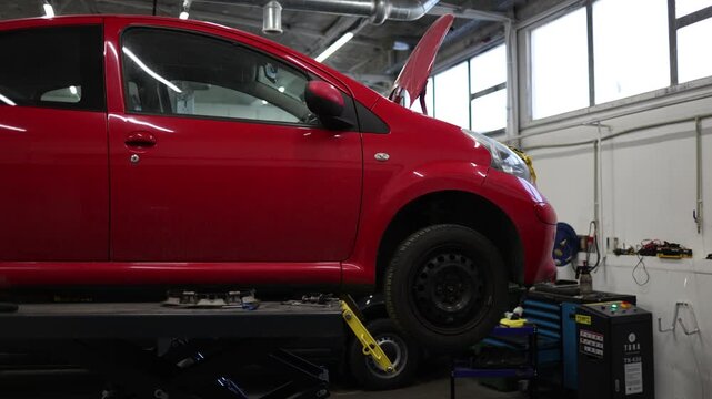 red automobile in a repair garage with the hood raised while mechanics perform diagnostic procedures and maintenance operations