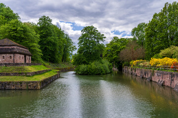 Fototapeta premium Colorful flowers and lush trees line a historic moat, creating a picturesque scene at Kurpark in Bad Pyrmont, Germany.