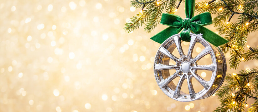 Banner Chrome car wheel with green ribbon on spruce branches on a background of golden festive lights with space for text. New Year's for tire shops, car dealerships, and auto repair services