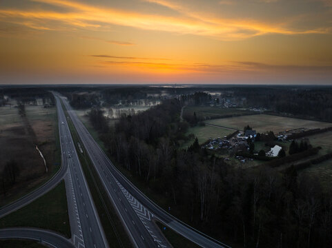 Aerial view of the highway intersection between the A5 and A8 roads surrounded by forests and fields during a golden sunrise in Olaine parish, Olaine Municipality, Latvia.