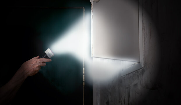 Hand holding flashlight inspecting electrical fuse box in a dark room