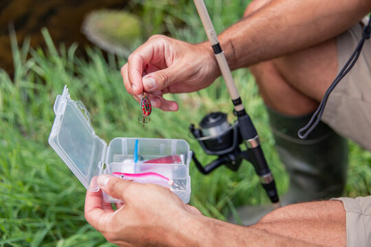 Fisherman selecting fishing lure from tackle box near river