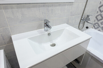 Fototapeta premium compact white rectangular sink with chrome faucet sits atop minimalist vanity. light gray stone-effect tiles and geometric accent panel frame modern bathroom corner