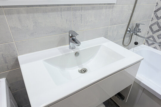 compact white rectangular sink with chrome faucet sits atop minimalist vanity. light gray stone-effect tiles and geometric accent panel frame modern bathroom corner