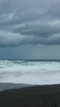 Vertical video: Rolling swells driving rough surf pushing foam onto shore during storm