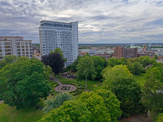 Fototapeta premium Manor park in Sutton town center, Greater London, UK. Aerial view above green public park with trees on a cloudy day. High rise apartment building. View towards high street with shopping center.