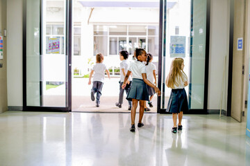 Fototapeta premium Children in school uniforms walking through a bright hallway.