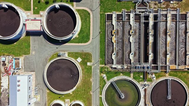 Aerial view of a wastewater treatment facility with large circular tanks and rectangular treatment systems. The site is busy with equipment and structures involved in water purification.
