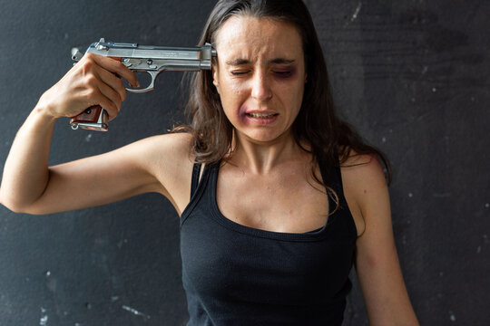 Woman with bruises holding a gun to her head, appearing distressed.