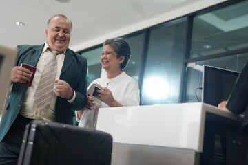 Fototapeta premium Passengers present documents to staff at an airport check-in counter while handling their luggage before a flight.