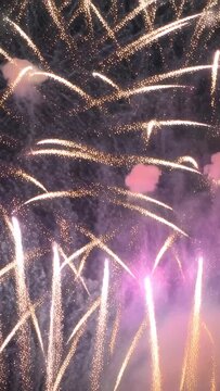 Vertical video: Launching aerial shells sending bursts and comet trails across night sky with smoke