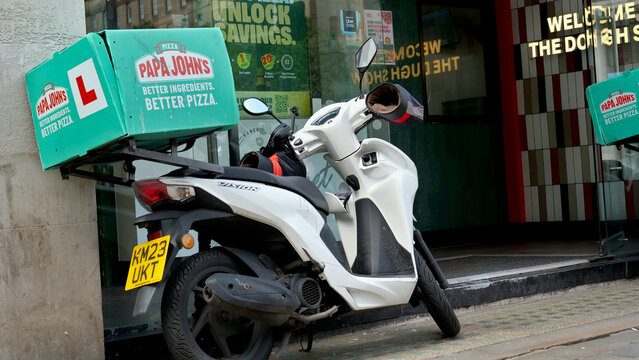Manchester, England, UK - 18 June 2026: Papa Johns pizza delivery scooter parked on street, fast food takeaway moped with green thermal box