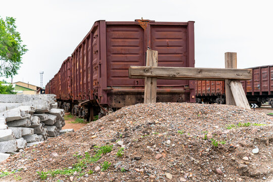 Rusty freight train cars standing on the tracks behind a pile of gravel and a wooden buffer stop.