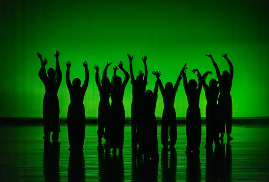 Dancers silhouetted on stage raising hands in unity