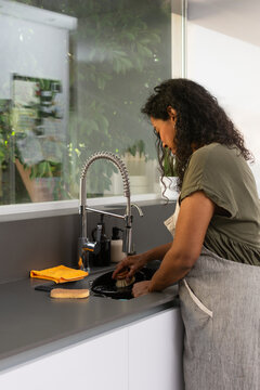 Woman cleaning cast iron pan with eco brush in modern kitchen sink
