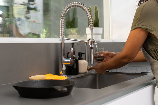 Woman filling glass with water at kitchen sink close up