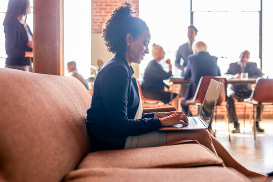 Woman working on a laptop in a modern office with colleagues nearby.