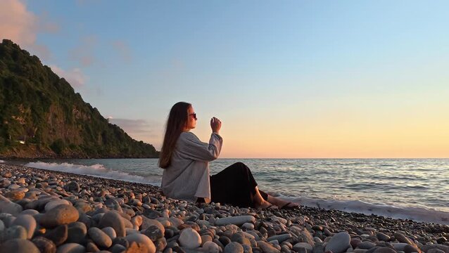 Young woman relaxing by the sea during sunset on pebble beach