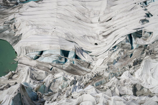 Aerial view of the Rhone Glacier covered with protective white blankets to prevent melting, with glacial ice and meltwater visible in Obergoms, Valais, Switzerland.