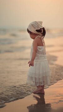 Cute little Asian girl walking on sandy beach at sunset, happy child enjoying tropical sea view during golden hour, family travel vacation, outdoor learning, active childhood growth and parenting