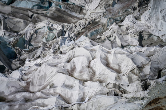 Aerial view of the Rhone Glacier covered with protective white fleece blankets to prevent melting, showing the textured fabric draped over the icy terrain in Obergoms, Valais, Switzerland.