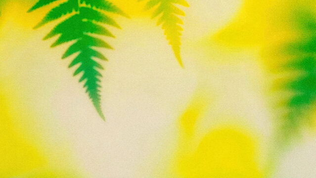 Green leaves create patterns on a bright yellow background in a natural setting