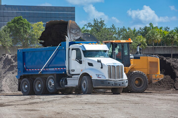 Front end loader filling a blue dump truck with soil at a construction site © Francisco