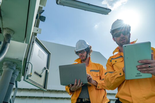 A maintenance engineer in a yellow jacket services telecom equipment on the building roof atop a commercial building, showing renewable energy, inspection and maintenance on a rooftop.
